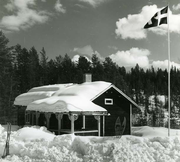 Albert Vikstens skrivartorp i Törn. I snödrivorna utanför står snöskor och skidor nedstuckna och flaggan är hissad.