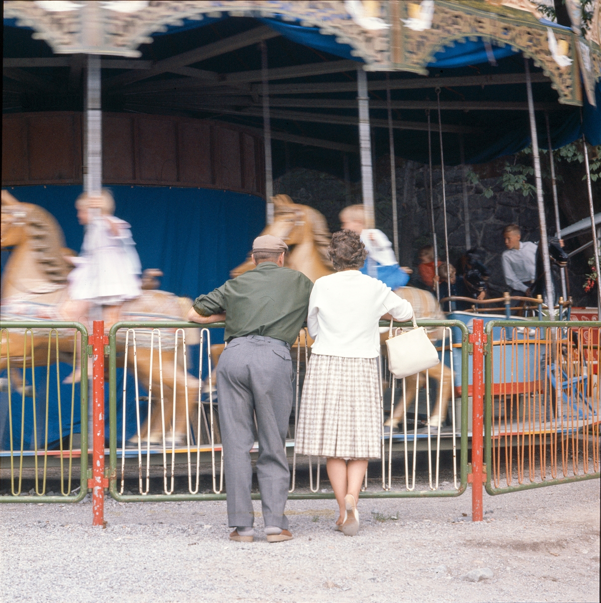 Ett äldre par betraktar barn som åker karusell.