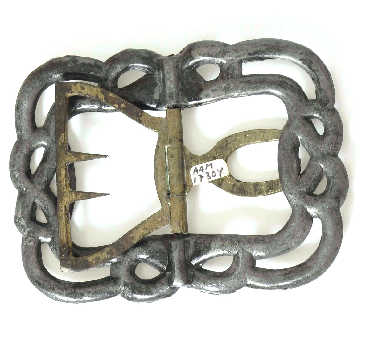Skospenne, i stål, med hekte av messing. Formet som 2 slyngende bånd  med opphøyde knopper  i kringleform midt på hver side.  

Fra  mannssko, svart,
