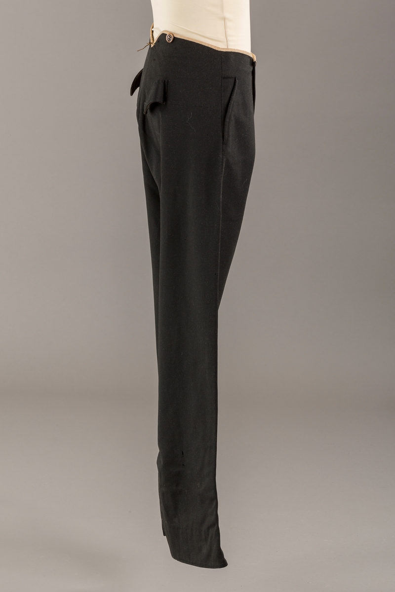 Form: Bena utvidet nederst. Lerretskant rundt livet, spensel i ryggen, mangler spenne i sepnsel?
Delvis foret. To lommer. 5 knapper, mangler en knapp.