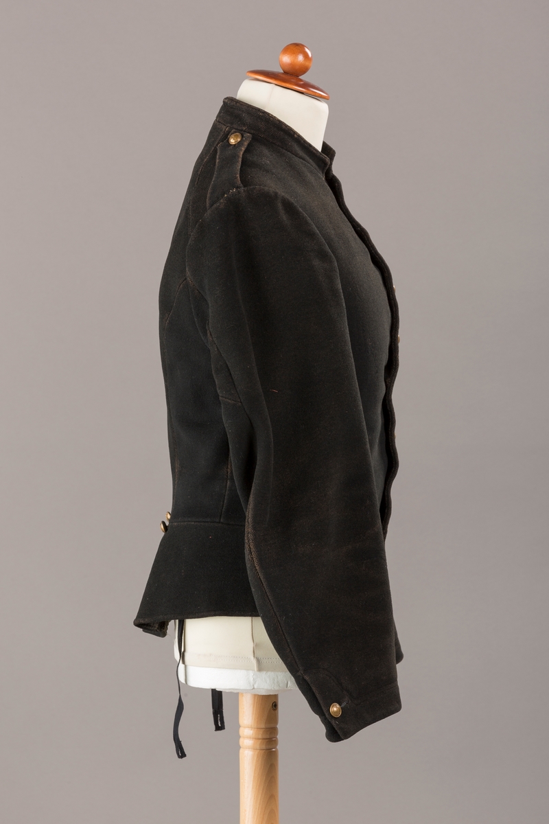 Form: Enkeltspent.

Foret med lin. Forsterket med silke på et lite stykke på ryggen. 12 messingknapper med mønster og tallet 1. Hempe i lin. Bendelbånd med knappehull.