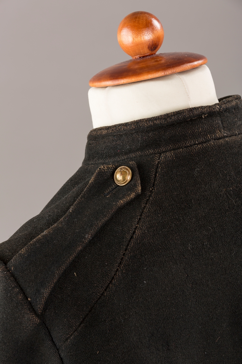 Form: Enkeltspent.

Foret med lin. Forsterket med silke på et lite stykke på ryggen. 12 messingknapper med mønster og tallet 1. Hempe i lin. Bendelbånd med knappehull.