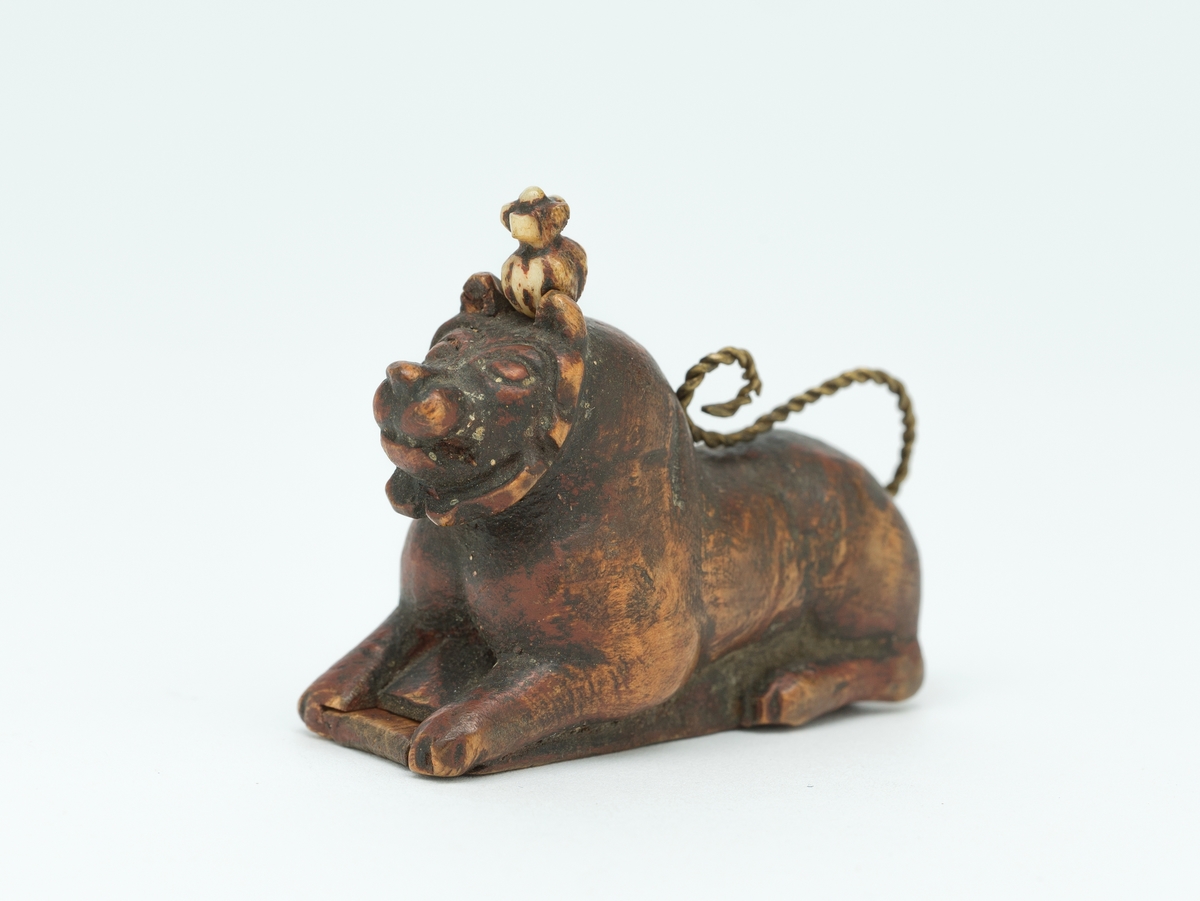 Liggende løvefigur av tre med snodd messingtrådshale. Lokk i bunnen.