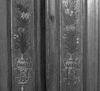 Ståndskåp med svängt, profilerat krön efter rokokoförebilder. 2 höga speglar med målad dekor i form av urnor med blommor, bl.a. pingstliljor, i rött, vitt, grönt mm.