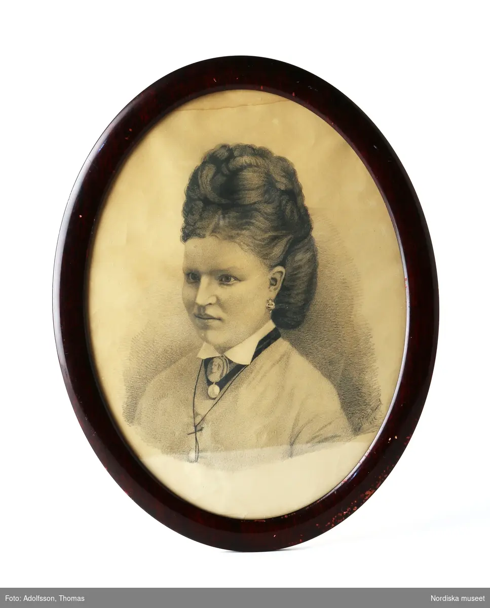 Porträtt, pennteckning, föreställande Augusta Lagerhall (1854-1931) vid 18 års ålder. Signerat i teckningens nedre högra hörn: "Carl Wetterstrand/1872".  I oval, glasad ram av mörkbetsat lövträ. Bakstycke av kartong, med blyertspåskrift: "Augusta Lagerhall/vid 18 års ålder"
/Anna Womack 2015-09-25