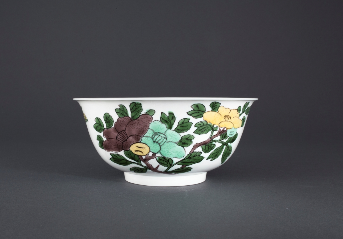 Oveglasur på hvit bakgrunn. Overglasurdekor: To grupper med  hibiskusblomster i pastell lavendlgrå, pastell turkis og pastell sitrongul med blader i en kraftig grønnfarge. Mellom de to blomstergruppene er sommerfugl som reflekterer fargene i blomstene. I godset under hver blomstergruppe er det innrisset en drage.