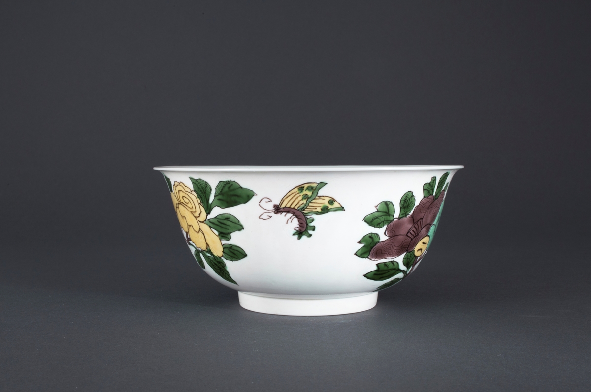 Oveglasur på hvit bakgrunn. Overglasurdekor: To grupper med  hibiskusblomster i pastell lavendlgrå, pastell turkis og pastell sitrongul med blader i en kraftig grønnfarge. Mellom de to blomstergruppene er sommerfugl som reflekterer fargene i blomstene. I godset under hver blomstergruppe er det innrisset en drage.