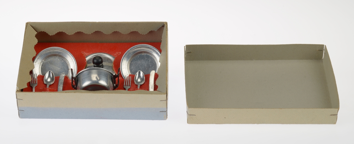 Et kjøkkensett som er montert i en liten pappeske med lokk. Settet er trolig fabrikkprodusert. Gjenstandene er undernummerert 01-10.
FTT.54457.01: En kasserolle med lokk laget av blikk. I hver side av kasserollen er det relativt store svartmalte håndtak av metall, og på lokket er det en treknott som også er svartmalt. Håndtakene og knotten er loddet på. Kasserollen er trolig valset.
FTT.54457.02-03: To identiske tallerkener laget av blikk. De er runde med en bred rand.
FTT.54457.04-05: To identiske kniver laget av metall, og de er antageligvis støpt. Håndtaket har prikker langs kanten som står opp fra metallet, og i midten er det en opphøyet stripe av metall. Knivbladet er relativt bredt og avrundet i tuppen. 
FTT.54457.06-07: To identiske skjeer laget av metall, og de er antageligvis støpt. Håndtaket har prikker langs kanten som står opp fra metallet, og i midten er det en opphøyet stripe av metall. 
FTT.54457.08-09: To identiske gafler laget av metall, og de er antageligvis støpt. Håndtaket har prikker langs kanten som står opp fra metallet, og i midten er det en opphøyet stripe av metall. Gaflene fire tenner.
FTT.54457.10: Esken der gjenstandene 01-09 er montert i. Esken og lokket er laget av papp og er stiftet i hjørnene. Esken er grå og blå på farge. Langs kanten inni esken er det klippet ute en tungekant. I bunnen er det en rød papplate der det er klippet ut hull for montering av de ulike gjenstandene.