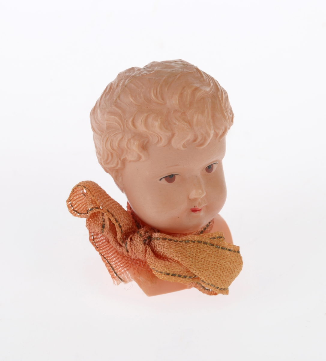 En liten komse med en pute og et dukkehode i. Gjenstandene er undernummerert 01-03. 
FTT.54491.01: En liten komse laget av et uthulet stykke tre som er kledd med garvet reinskinn. På kalesjen er det dekorert med røde pyntebånd av ull festet på et gult bånd av ull. Det er også to flerfargede dusker på kalesjen. i kalesjen er det festet et tvunnet ullbånd som er festet i den andre enden av komsen slik at man kan bære den. Det er også sydd på et pyntebånd i gult og rødt på oversiden.
FTT.54491.02: En liten rød pute sydd av silkestoff som ligger inni komsen.
FTT.54491.03: Et dukkehode laget av plast som ligger i komsen. Håret er støpt og er krøllete. I ansiktet er det malt på øyne og munn. Rundt halsen har dukken et silkebånd.