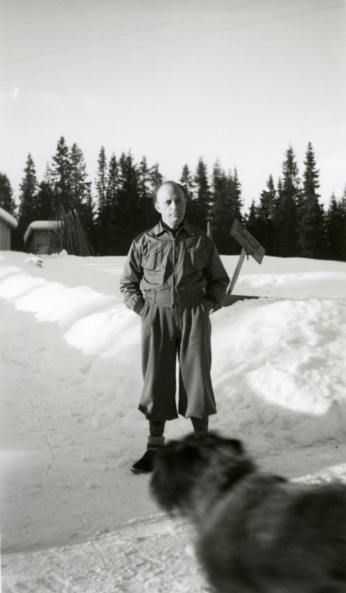 Haakon Garaasen (6/7 1887 - 1957) stående ute i snøen med hendene i bukselommene. Hund i forgrunnen.