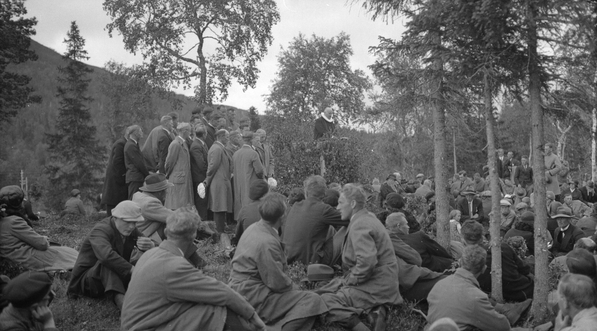 Bondestevne på Majavatn på 1934. Mye folk sittende i skogen. Prest på talerstol.