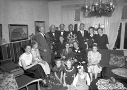 Pent kledte menn, kvinner og barn samlet i en stue. Fra Nord