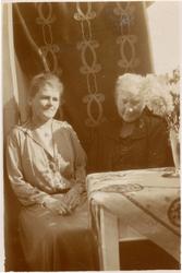 Portrett, To kvinner sitter i stue. Broderte gardiner, bord 