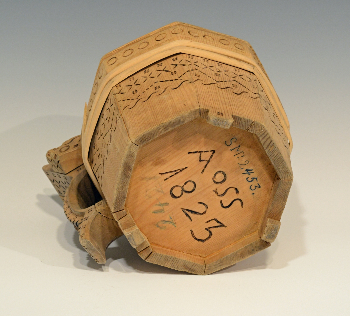 Fra katalog: Ottekantet smørkande og stav med hank og laak og tre smaa føtter, utvendig svimerket og en slynget ring oppe paa laaket, indvendig
rik rosette. Under staar brændemerket: A OSS 1823,