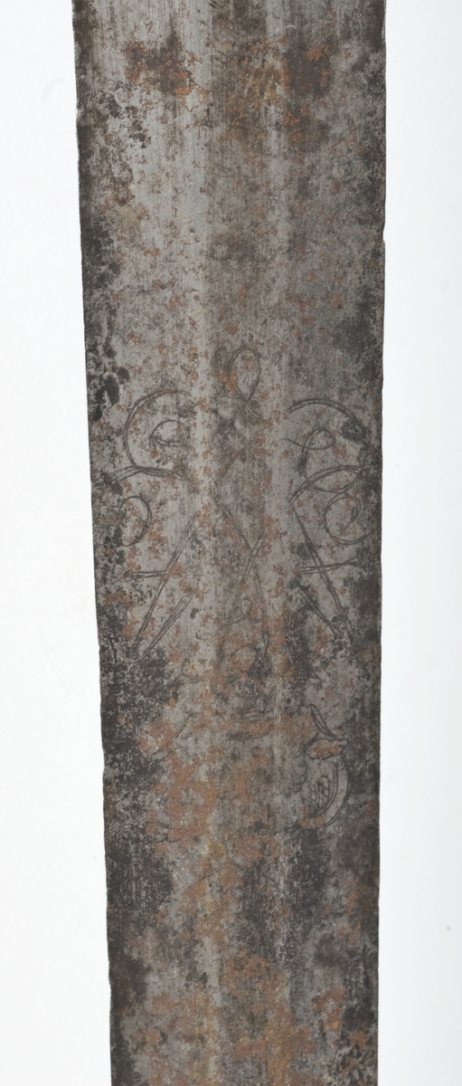 Dansk/Norsk Soldatkårde modell 1701. Plommeformet knapp med nitteknapp. Tregrep med messingtråds bevikling og hylse oppe og nede. Nyreformet parerplate med 7 fliker. Nedbøyd bakre parerstang. Fremre parerstang går over i håndbøylen og er tappet i knappen.
Rett tveegget klinge med 6 kantet tverrsnitt. Klingen er etset med Fredrik 4's speilmonogram på begge sider.