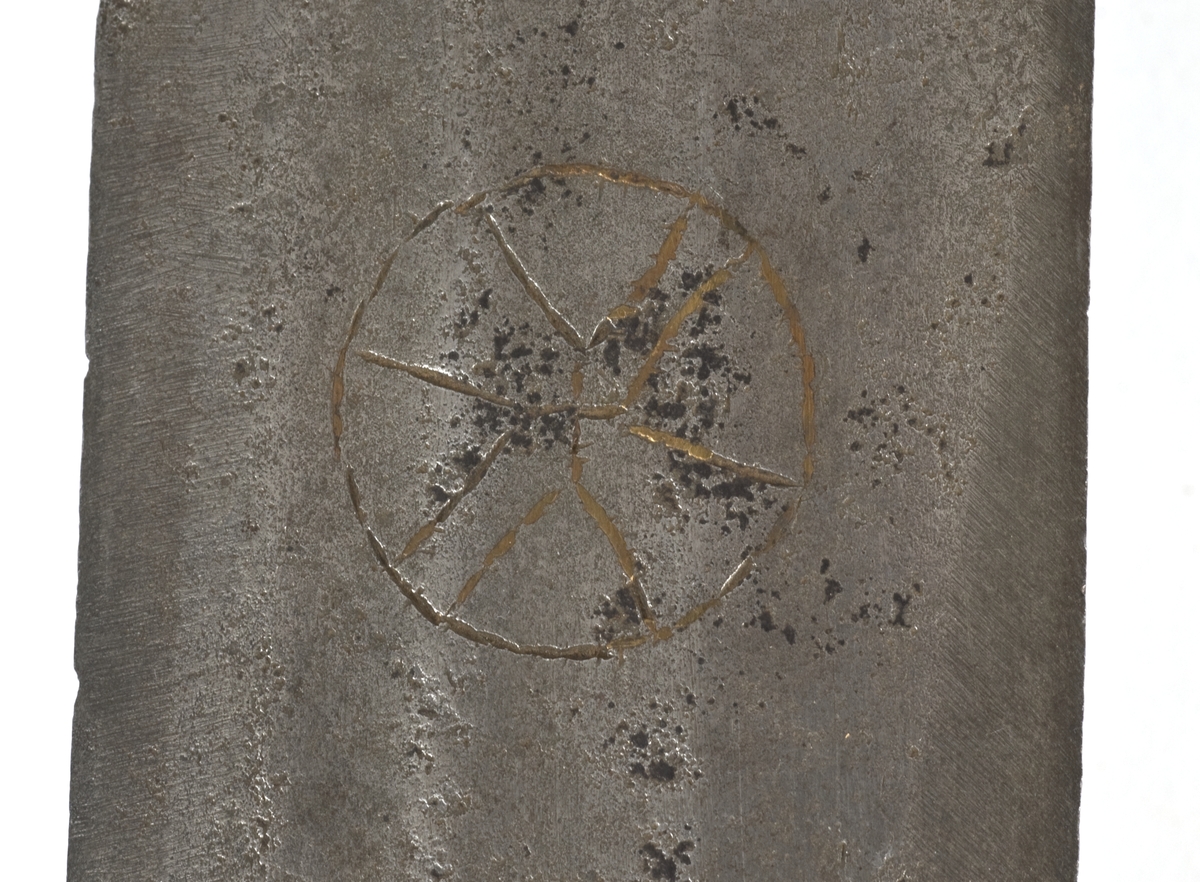 Fasettert rundt knapp med 8 fasetter. Det er innslått 4 smedmerker på knappen, i annethvert felt. Tregrep  Asymerisk åpen parerring med  bøyler med rektangulært tverrsnitt og med kringlefasong med en ytre og en indre parerring. Ytre ring har utsmidde rektangulære partier med kryssfliling. Ytre og indre ring er låst ved at de er tvunnet sammen i senter. Utsiden er smidd som en plateformet deksel. Denne typen pareranordning er trolig norsk
Bred tveegget klinge med 3 brodrender på hver side. Klingen er merket med  Solingens løpende ulv, et hjul og 2 andre symboler på begge sider. Klingen er brukket.