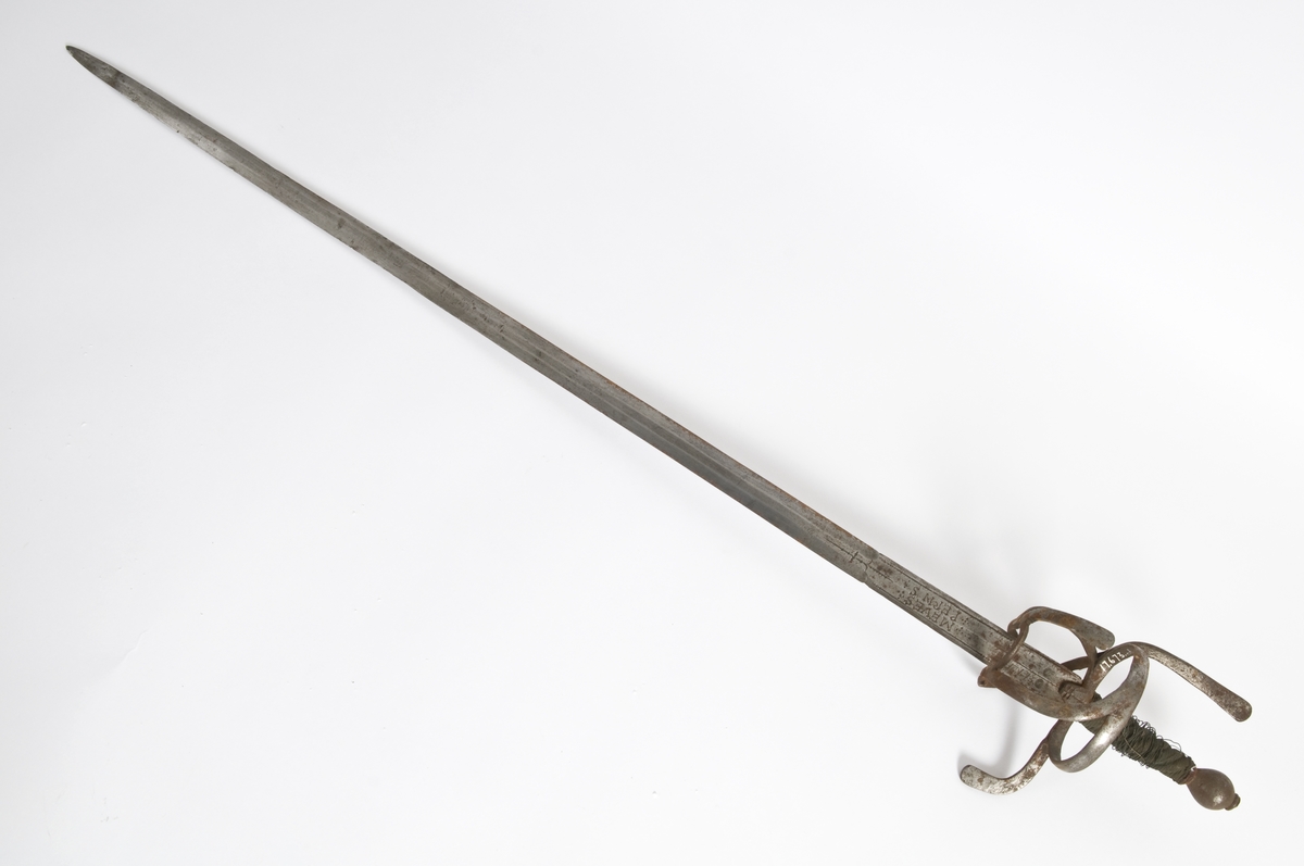 Pæreformet knapp. Tregrep med mssingtråds bevikling og tyrkerhode oppe.. Asymmetrisk feste med flate bøyler. Fremre parerstang går over i håndbøylen. Sidering. Flere bøyler av festet på innsiden er borte. 
Tvenegget, rett klinge med sekskantet tverrsnitt. og 2 korte brede blodrender på hver side.. Klingen er merket med  bokstavene MEVES PERNS på begge side i blodrendene. To smedmerker på hver side " lpende hjort "