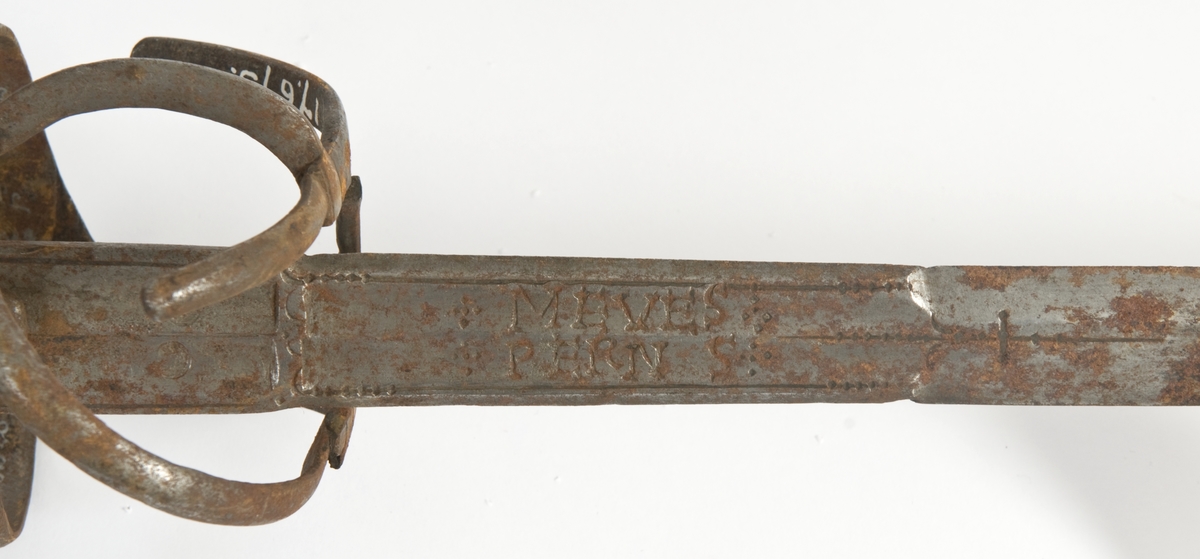 Pæreformet knapp. Tregrep med mssingtråds bevikling og tyrkerhode oppe.. Asymmetrisk feste med flate bøyler. Fremre parerstang går over i håndbøylen. Sidering. Flere bøyler av festet på innsiden er borte. 
Tvenegget, rett klinge med sekskantet tverrsnitt. og 2 korte brede blodrender på hver side.. Klingen er merket med  bokstavene MEVES PERNS på begge side i blodrendene. To smedmerker på hver side " lpende hjort "