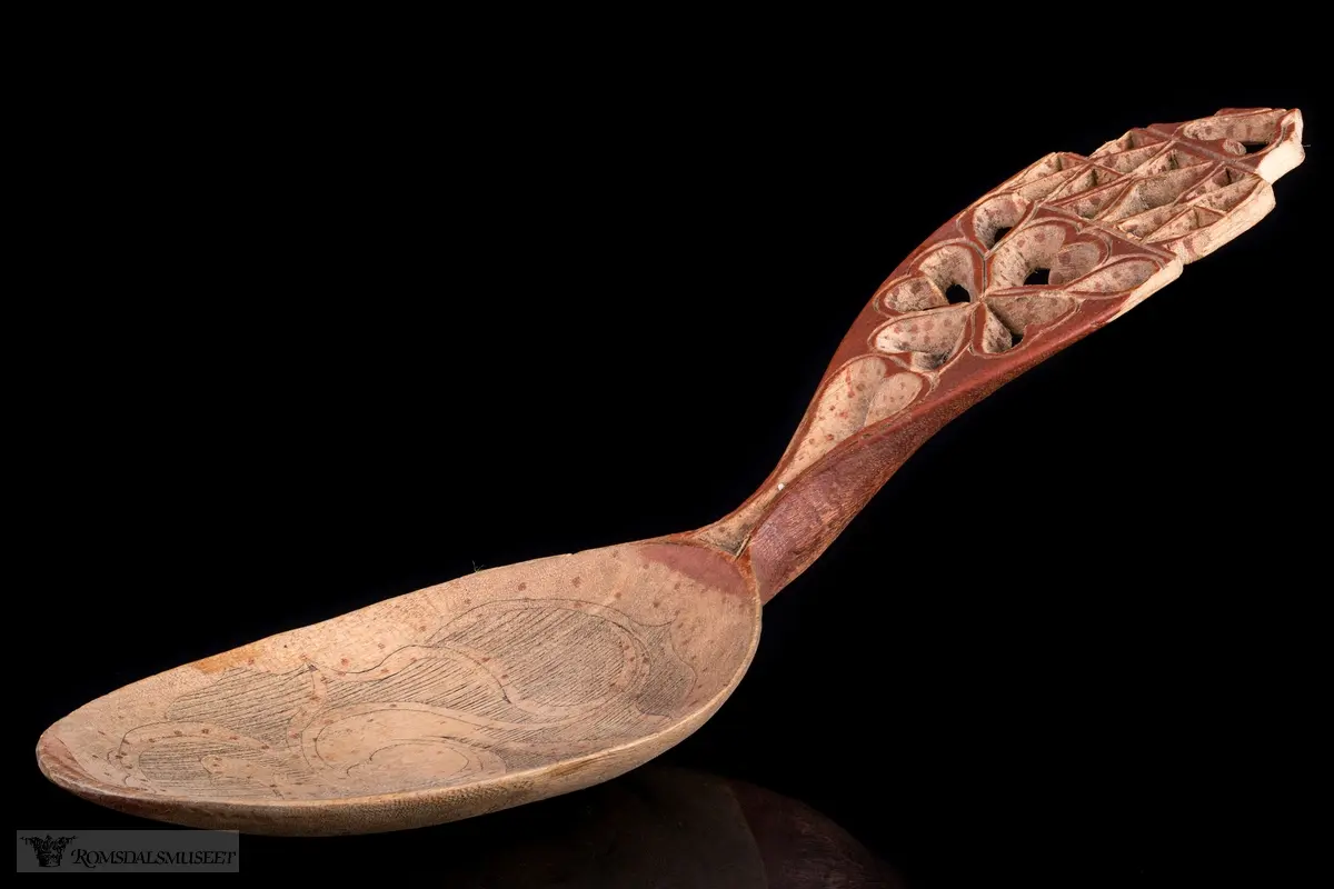 Skaftet perforert,-hjertering, selve skjeen abstrakt flate- og liljemønster med røde prikker.