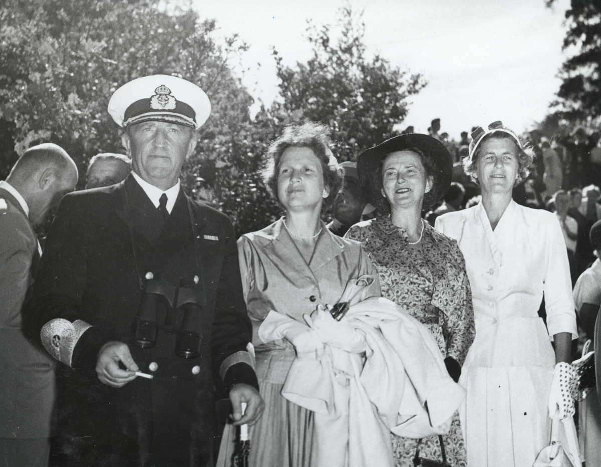 Konmteramiral Samuelson, klädd i uniform och med en kikare runt halsen, står tillsammans med tre uppklädda kvinnor. Bilden är tagen i samband med "Operation kullen" 1955.