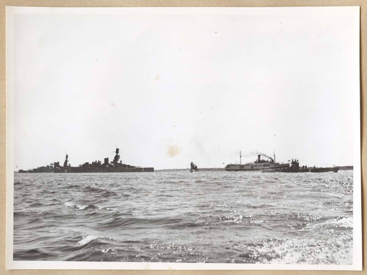 Till sjöss syns pansarskeppen Gustav V samt Sverige (efter ombyggnaden 1945), Lasarettfartyget Prins Carl och en Ubåt. I bakgrunden skymtar land.