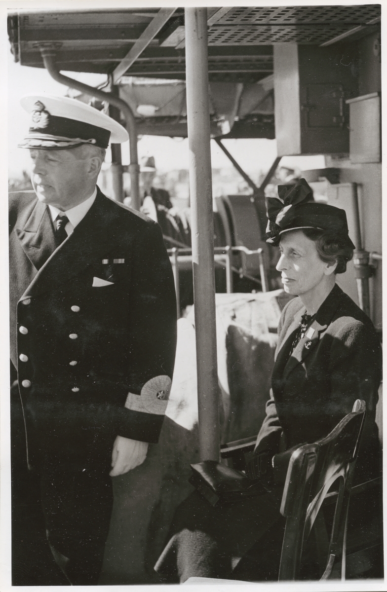 Drottning Louise sitter ned ombord på ett fartygsdäck. Vid sidan om henne står Konteramiral Ehrensvärd.