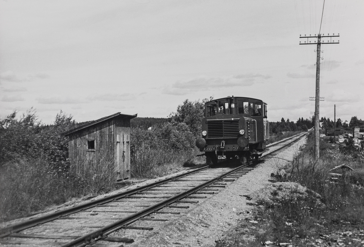 Fra Vestmarkalinjen, eller Paradisbanen som den også ble kalt, siste driftsdag, 10.07.1965. En skiftetraktor er underveis fra Skotterud til Buåa for å hente lastede vogner.