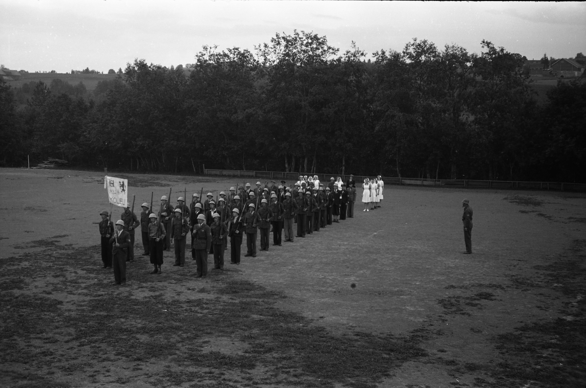 Milorggruppa på Kolbu (HS1432-4), samt lotter, deffilerer på Kolbu Idrettsplass, trolig i forbindelse med et arrangement i anledning Milorgs demobilisering i juli 1945. Åtte bilder.