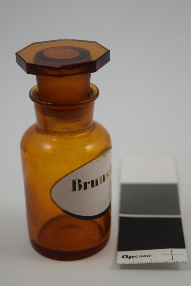 Brun glasskrukke med glasspropp. Etikett hvit med sort skrift. Har inneholdt brunsten, som er Manganoxyd. Brukes i kjemiske reaksjoner og analyser. Teknisk.