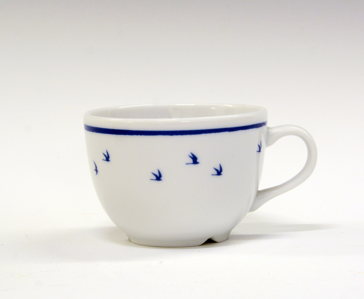 Kopp av porselen med hvit glasur. Dekorert med blå strek og blå flyvende fuglesilhuetter.
Modell: Roma