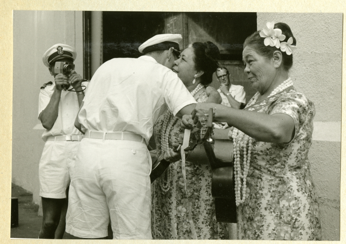 Bilden föreställer en besättningsmedlem i vit sommaruniform som kramar om en kvinna. I bakgrunden syns ytterligare en besättningman som fotograferar händelsen. Bilden är tagen i samband med minfartyget Älvsnabbens långresa 1966-1967.