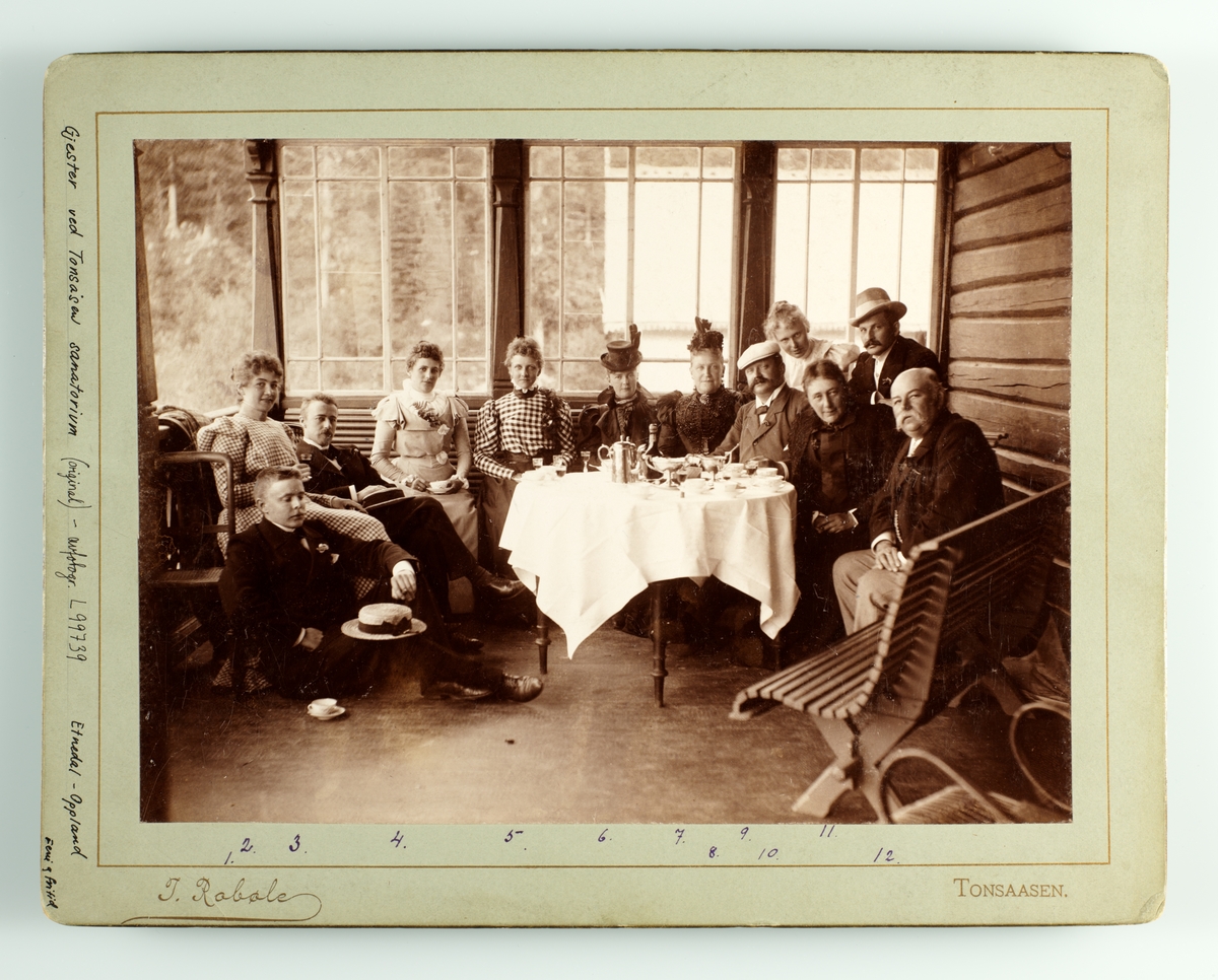 Tonsåsen sanatorium, gruppe gjester samlet rundt dekket bord på åpen veranda. Kaffe- og alkoholservering på hvit duk. Trebenk mot veggen. Navneliste, se Eks.3, påskrift.