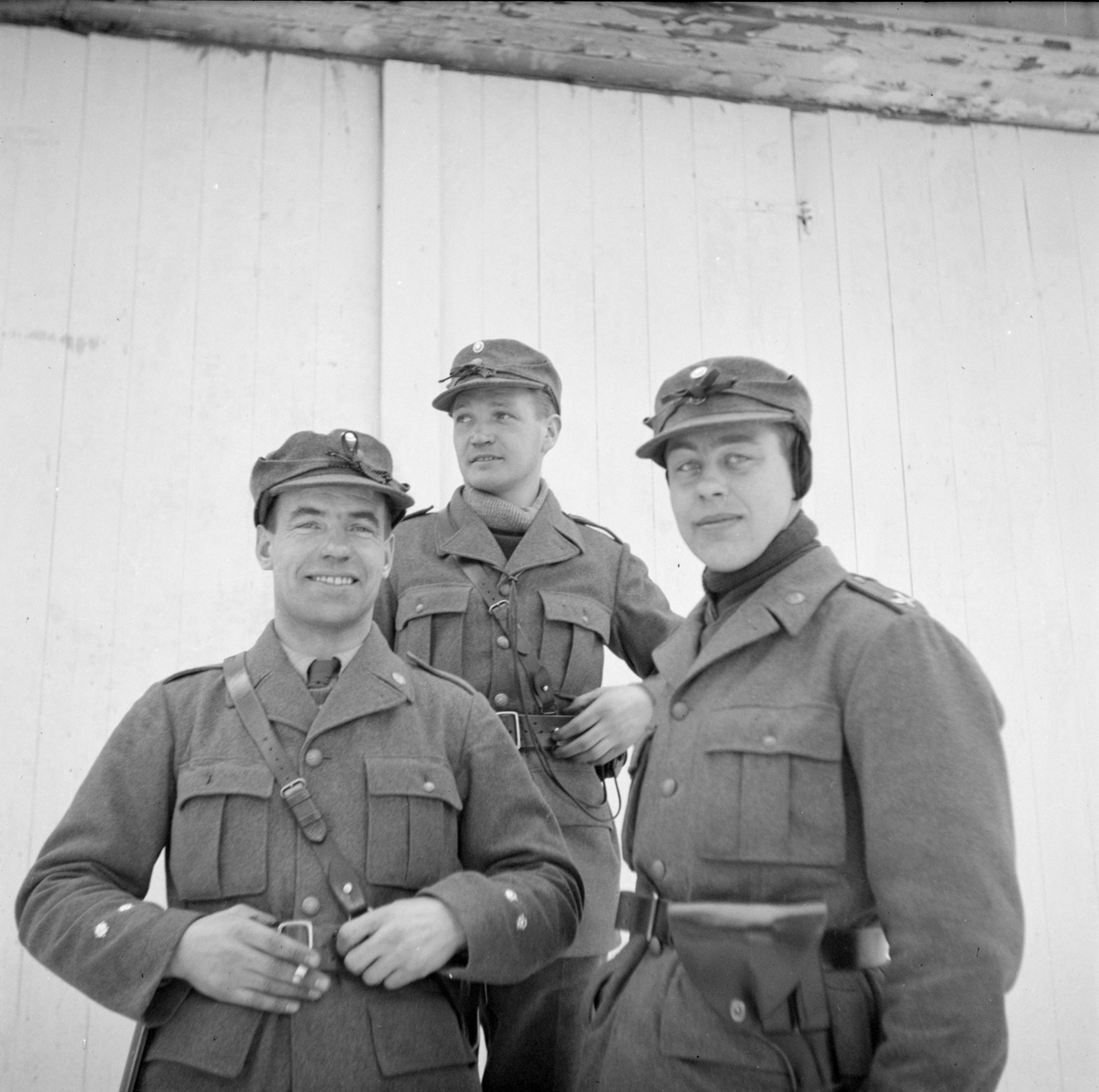Grupporträtt. Tre militärer tillhörande Svenska frivilligkåren i Finland, F 19, står vid en husvägg.