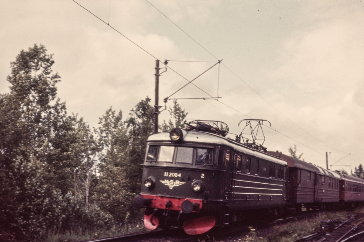 Ekspresstog fra Stockholm til Oslo Ø passerer ved Bingsfoss mellom Blaker og Sørumsand. Toget trekkes av elektrisk lokomotiv El 11 2084.