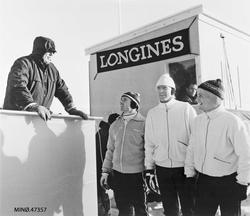 Kong Olav V på tribunen. Skiløpere