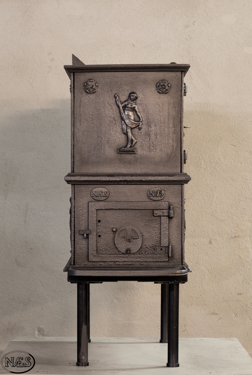 Kokeovn i to etasjer med eget fyrkammer og kokerom. Kokerommet kan åpnes med to dører på langsiden og med en luke i topplaten. Ovnsdøren til fyrkammeret er på kortsiden 1 etg. På langsidene i 1. etg er det tre muser og en engel med lette draperier på en enkel profillist. På kortsidene 2. etg er det draperikledd dansende muse på enkel profillist med en rosett i hvert øvre hjørne. Langsidene i 2.etg er dekorert med en rosett i hvert øvre hjørne.