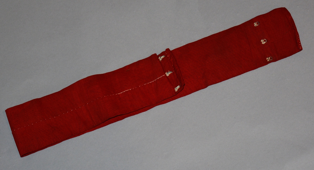 Rødt, rektangulært uniformsbelte som lukkes med hemper.