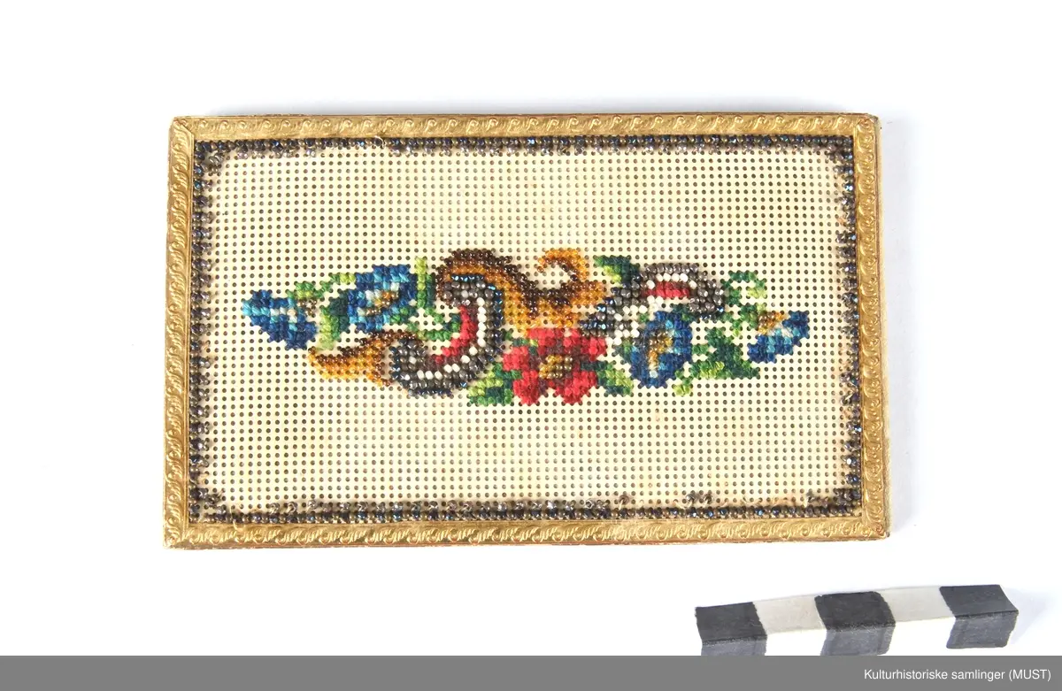 Visittkortmappe av papp. Permene består av hvit, perforert pappkartong og hvit silke. På permene korsstings- og perlebroderier, langs kanten en "gullist".