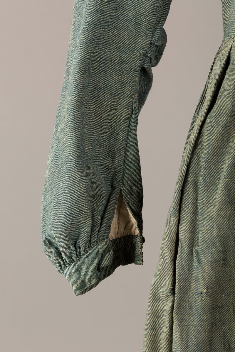 Form: Trangt liv med legg foran, skjørtet sydd med legg i livet.  God vidde i skjørtet, lange armer. Fem hekter i livet mangler.