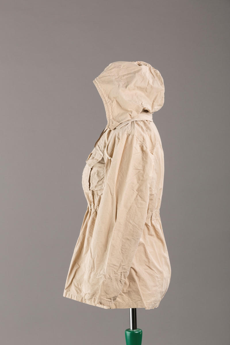 Form: Vanlig anorakkfasong med strikk i livet. 2 brystlommer med knapp.
Hette med glidelås på topp midt, snøring.
Glidelås helt ned foran.
Innermansjett med strikk i ermene.