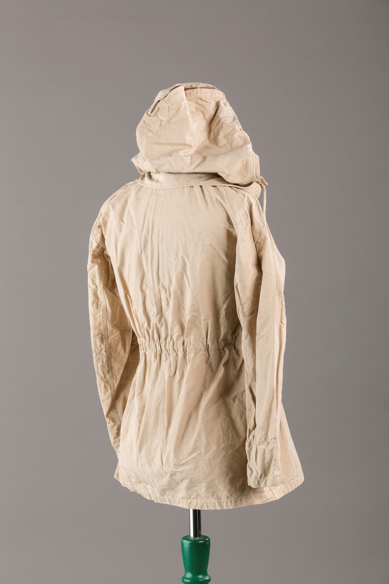 Form: Vanlig anorakkfasong med strikk i livet. 2 brystlommer med knapp.
Hette med glidelås på topp midt, snøring.
Glidelås helt ned foran.
Innermansjett med strikk i ermene.