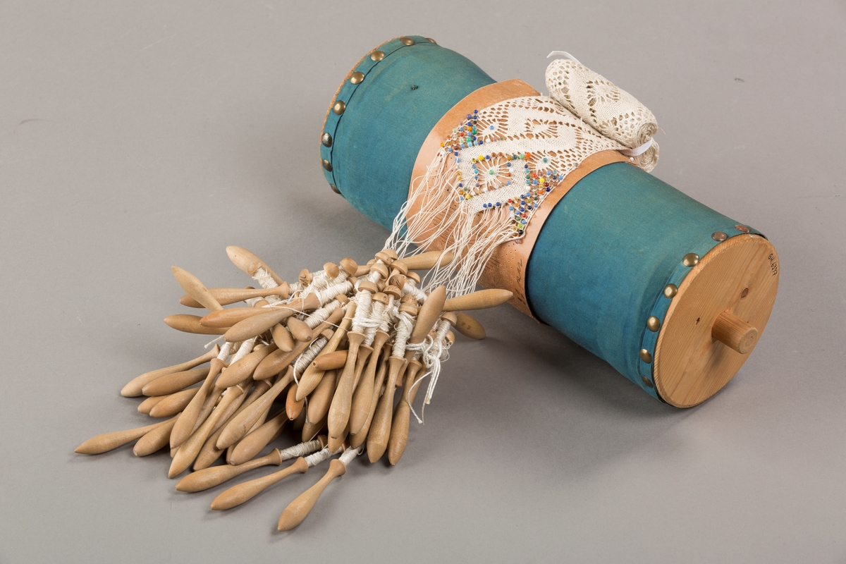 Form: Sylinderformet "pute" hvor stivt pappstykke rundt puta viser mønsteret. 
Kniplingsstykke under arbeid påspent med knappenåler
Pinner medkniplingstråd