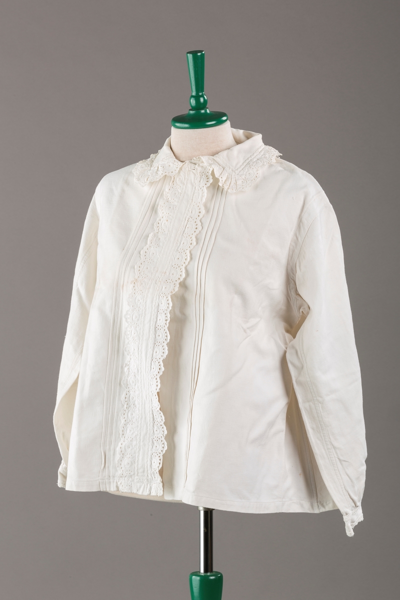 Form: Hoftelang trøye, Lange ermer, krage. Kragen og åpningen foran er kantet med  maskinprodusert blonde. Tre biser på hver side av åpn. foran. Lukkes med to løse knapper.