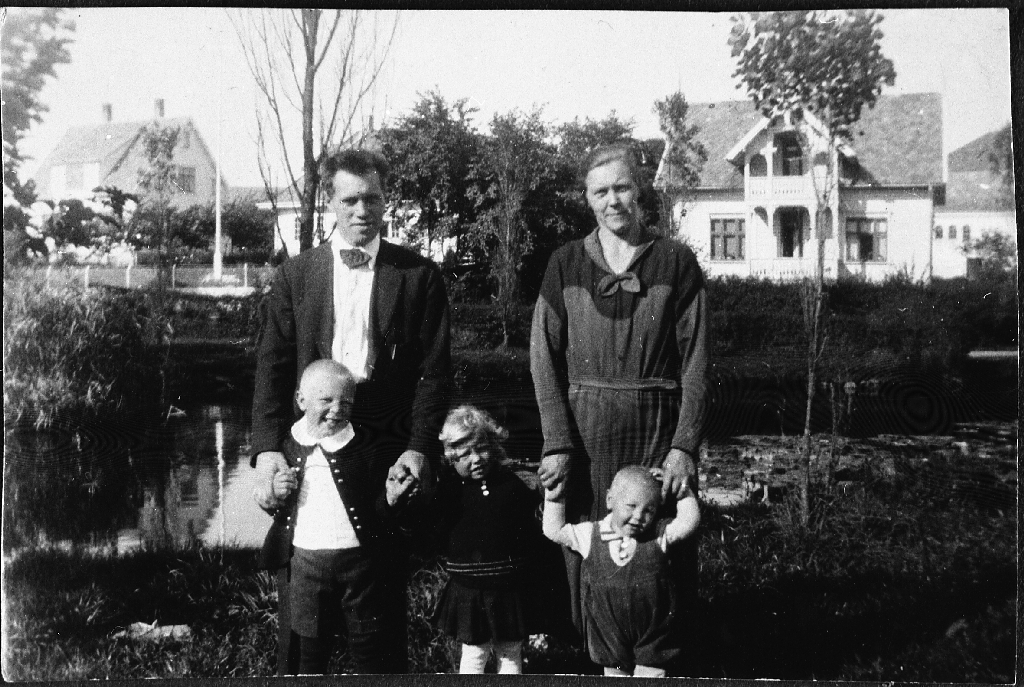 Familien Ueland på torget. Bak f. v. Teodor Ueland 25.9.1897 - 15.8.1990), Bergit Ueland f. Rossnes (25.12.1903 - 28.4.1965). Framme f.v. Arne Gabriel Ueland 25.2.1929 - 29.3.1983), Anna Ueland g. Børresen (30.4.1930 - ) og Jørgen Ueland (23.3.1832 - 15.3.2011) Huset t.h. bak var matstova under krigen.
