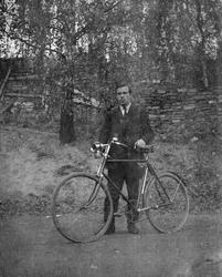 Pål Kluften står med sin sykkel på vegen med en høy steinlag