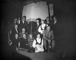 Gruppe mennesker samlet rundt peisen med Alfred Maurstad på 