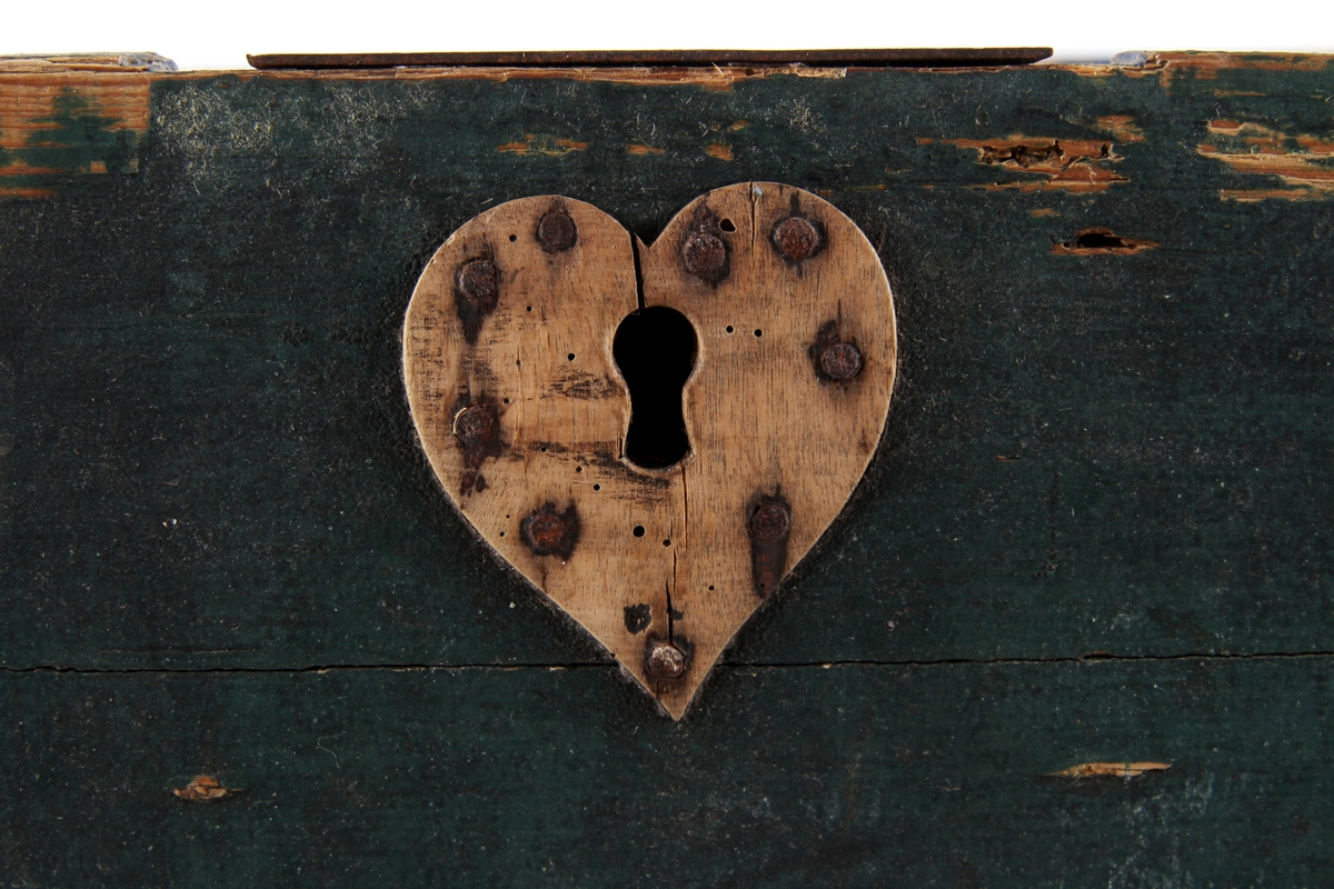 Grønnmalt trekiste med hjerteformet låsbeslag skåret ut i tre. Lås og hengsler i metall. Kisten har leddik med lokk innvendig.