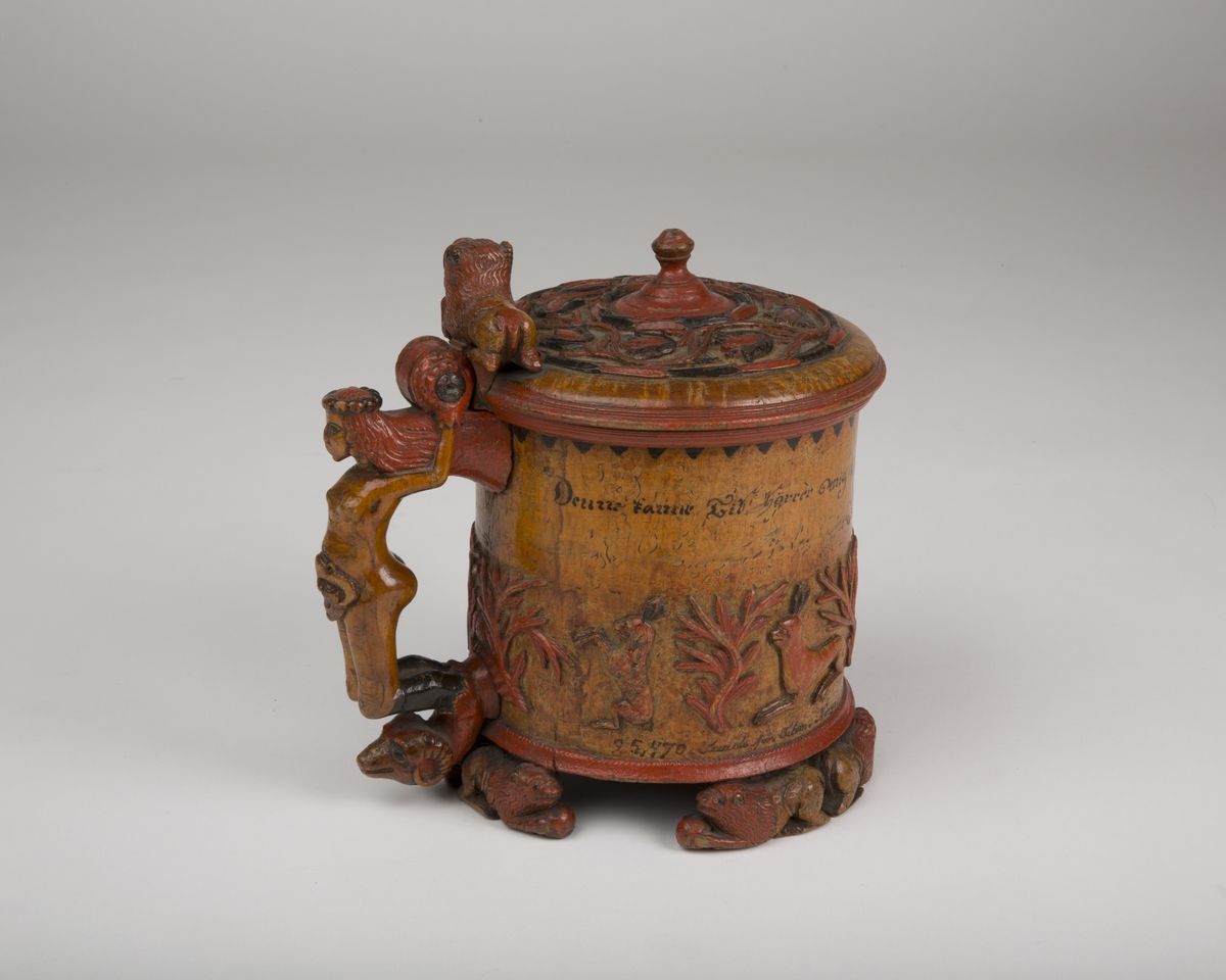 Dekorert med fortløpende billedfrise med dyr og trær på nederste del av korpus. Kannen har løveføtter og løvegjekk og bakkantine som håndtak. 