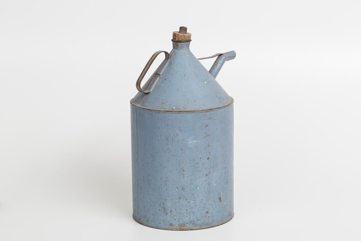 Kanne i sink, blå. Korket i tuten og korklokk med plast. Har håndtak og helletut. Kannen har påklistret god jul merkelapp med navn. Delvis avrevet.