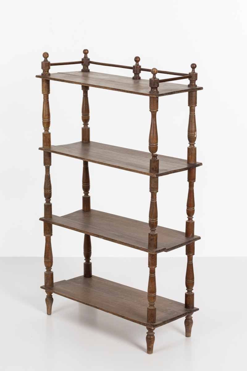 Hylle med 4 hyller. Dreide stolper mellom hyllene. Mangler ett bein. Sprosser øverst. Lakkert i mørk brunt.